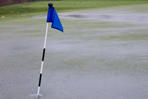 Rain storm saturates putting green with puddle water ending practice.