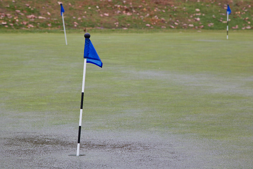 Rain storm saturates putting green with puddle water ending practice.