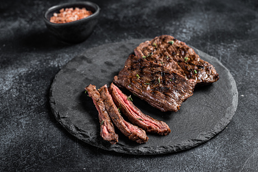 Traditional barbecue skirt steak sliced on a cutting board.  Black background. Top view.