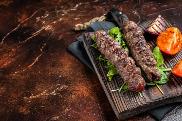 Turkish adana kebab, ground beef and lamb meat grilled on skewers  served with tomato, salad and onion. Dark background. Top view. Copy space.