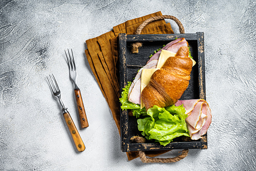 Fresh croissant sandwich with ham, cheese and salad leaf. Gray background. Top view.
