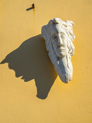 Rimini, Italy - August 02, 2022: Carved head on the wall of one of the buildings in the old part of Rimini, casting long shadow.