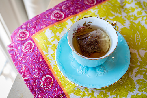 Herbal tea and the teabag in an elegant teacup and saucer on a colourful placemat