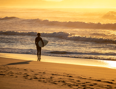 Silhouette of a surfer with a board on a sunset background.