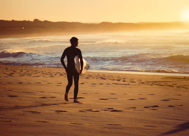 istock Surfer walking observing the surf on a beach at sunrise 1440849016