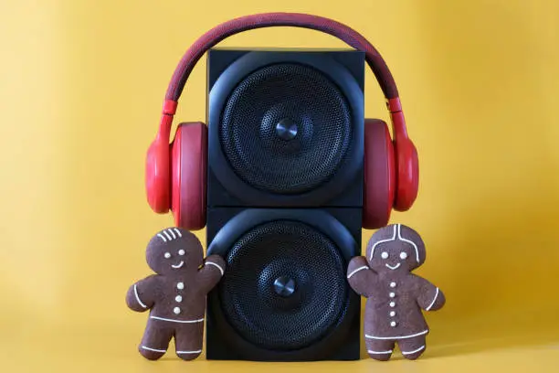 Photo of Two black audio speakers, red headphones and funny gingerbread men on a yellow background. Ð¡oncept of a holiday party, disco, pop music, family and children's audio broadcasts. Sound tower.