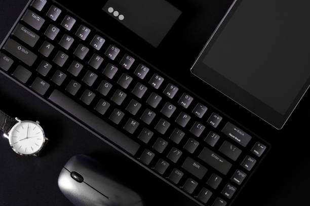 istock Small mechanical computer keyboard with 68 keys on a black background next to a wristwatch, a computer mouse, a tablet and an external ssd. Modern gadgets. 1440861525