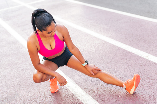latin sportswoman stretching legs on the athletics track during her training, concept of urban sport and healthy lifestyle, copy space for text