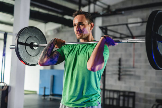 Partial front view with light effect of Caucasian man preparing to press barbell overhead in open plan gym.