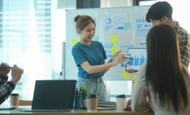 istock Two happy young colleagues standing  near whiteboard and presenting business plan, graph chart diagram at corporate meeting. 1440867121