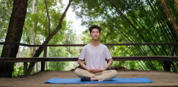 istock Young man practicing yoga and meditating at open yoga studio with beautiful nature view in background. 1440868338