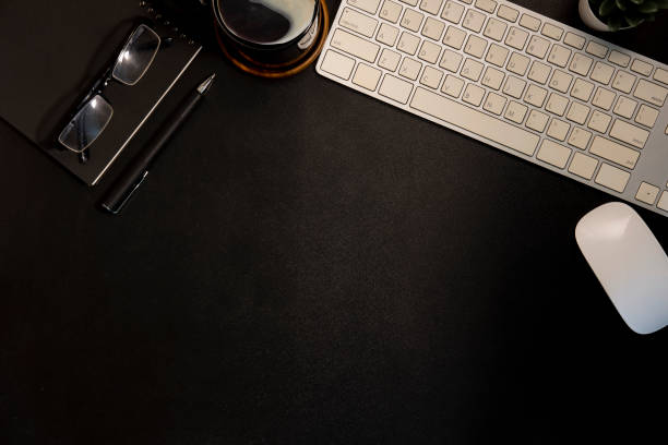 istock Flat lay wireless keyboard, coffee cup, glasses and stationery on black table. Top view with copy space. 1440868479