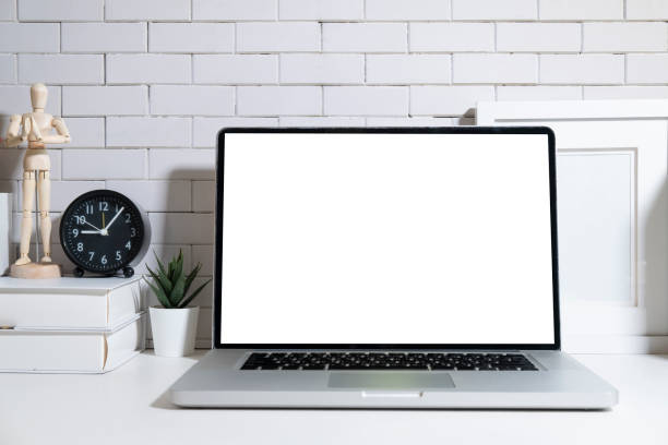 istock Front view laptop computer with blank screen, books, alarm clock and potted plant on white table. 1440868500
