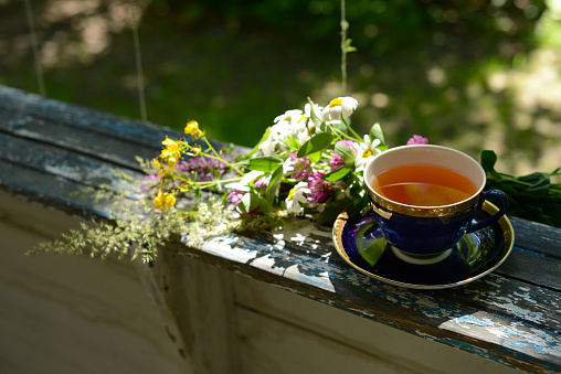Cup of tea and bouquet chamomile flowers and wildflowers on wooden table in garden, blurred background, soft focus