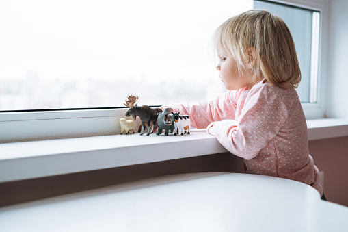 Little girl toddler playing with animal toys on table in children's room at home