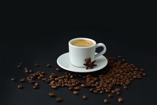 Black coffee and roasted coffee beans on table on a black background. Small cup espresso and anise star
