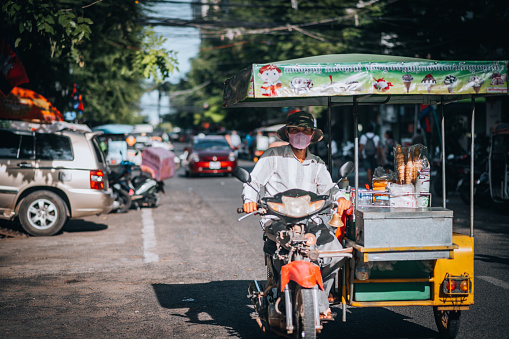 Cambodia, Phnom Penh, November 11, 2022. Man rides through the city with a motorcycle and sidecar loaded with vegetables