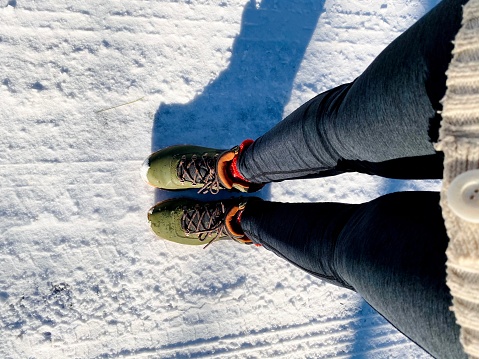 Looking down view of partial winter coat and legs and green hiking/snow boots on a snow covered road. Taken in Northern Wisconsin, USA.