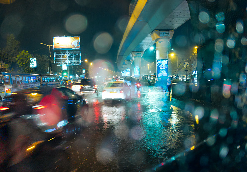 Kolkata, 09/08/2022: During a heavy monsoon rain, view of city traffic visble through a car window. Trailing of moving cars, glowing neon lights of advertising billboards and rain drops ... all creating a magical atmosphere.