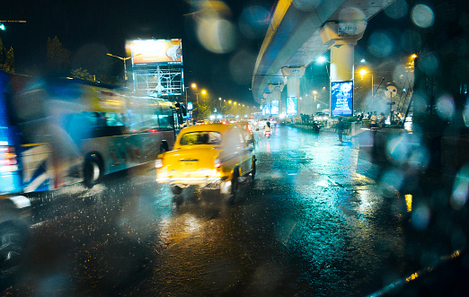 Kolkata, 09/08/2022: During a heavy monsoon rain, view of city traffic visble through a car window. Trailing of moving cars, glowing neon lights of advertising billboards and rain drops ... all creating a magical atmosphere.