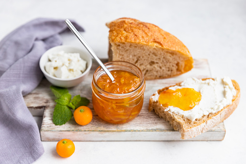 Sliced artisan homemade bread with ricotta or cottage cheese and orange jam on light grey background. Tasty breakfast. High key photography.