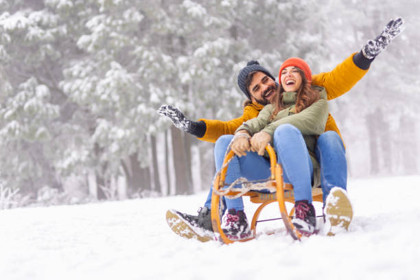 Couple having fun sledging while on winter vacation stock photo