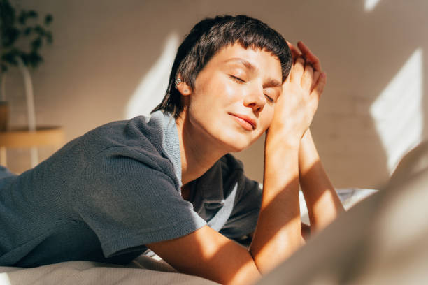 una donna giace su un letto alla luce del sole dalla finestra. - sensuality lifestyles cheerful comfortable foto e immagini stock