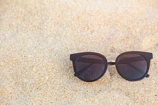 Sunglasses placed on the sand with nature reflection in polarized lenses and blurred sea view in the background