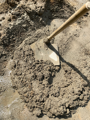 Stock photo showing close-up view of small pile of wet cement being spread over pavement with long handled concrete placer.