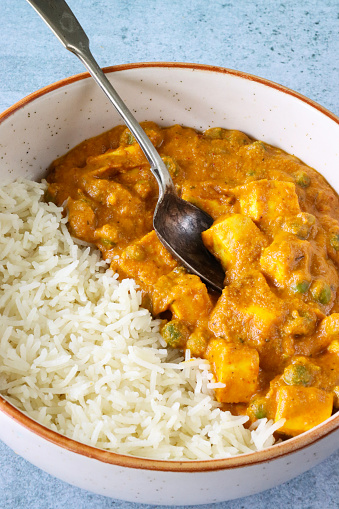 Stock photo showing close-up, elevated view of bowl containing a portion of Matar paneer served with white rice. This is an Indian vegetarian dish consisting of paneer, similar to cottage cheese, in pureed tomatoes with added green peas and flavoured with spices including garam masala.