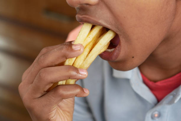 a teenage boy eating french fries while sited - child obesity imagens e fotografias de stock