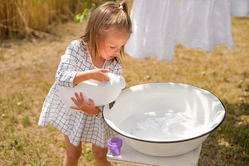 Cute beautiful little girl pours laundry detergent from a large white bottle. Safe bleaching of fabrics