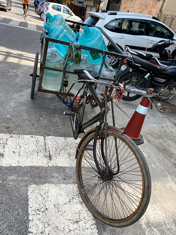 New Delhi, India - September 3, 2022: Stock photo showing close-up view of pile of empty, water cooler containers loaded in trailer attached to a bicycle parked in a residential district.