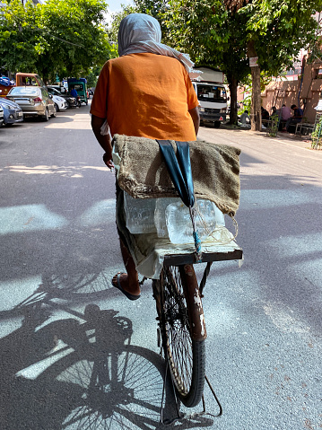 New Delhi, India - September 3, 2022: Stock photo showing close-up view of cyclist  peddling through a residential district to transport large blocks of ice to be sold to fishmongers.