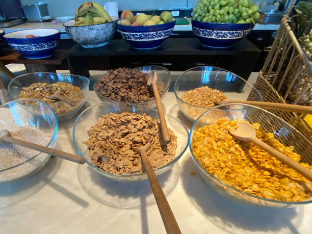 imagem em close-up da exibição do buffet de café da manhã de frutas e cereais em tigelas de vidro e porcelana, muesli, mingau de aveia, flocos de farelo, flocos de milho, uvas, bananas e maçãs, vista elevada, foco em primeiro plano - bran flakes - fotografias e filmes do acervo