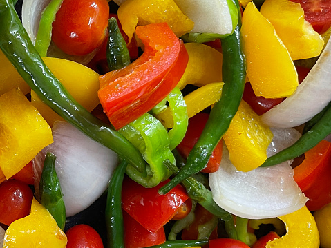 Stock photo showing close-up, elevated view of a frying pan with red and yellow bell peppers, green beans, onion, green chilli pepper, cherry tomatoes, ingredients for a stir fry. Healthy eating concept.