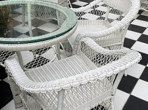 Full frame image of glass topped garden patio table with rattan wickerwork chairs outdoors, restaurant al fresco dining area, black and white checked tiled floor, focus on foreground
