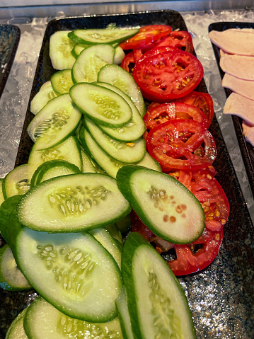 Stock photo showing close-up, elevated view slices of cucumber and tomatoes as part of salad bar restaurant buffet.