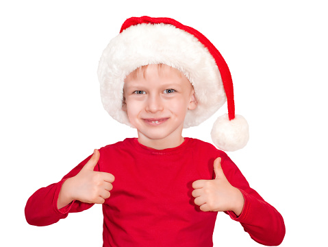 A child dressed in a red sweater and Santa Claus hat shows likes with two hands on an isolated background