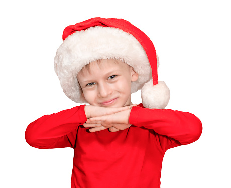 A child dressed in a Santa Claus hat and a red sweater folded his hands under his chin smiled and bowed his head to his side against an isolated background. High quality photo