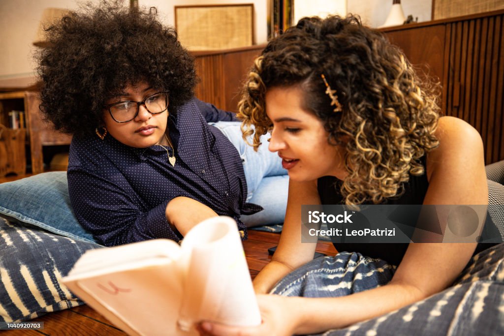 Young women reading together at the book club Teenage girls reading books together sitting on the living room’s floor. Female Friendship Stock Photo