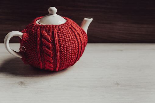 Red sweater cozy teapot on wooden background