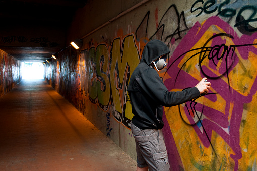 Masked Street Artist with Spray Can in a Tunnel. Milano Outskirts, Italy