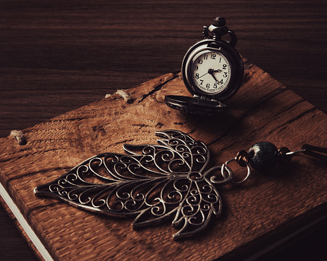 Closeup view of vintage pocket watch and leaf pendant on walnut wood background