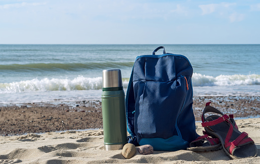 A thermos of tea and a backpack against the backdrop of nature. Drinking tea on the seashore. Walking along the seashore.