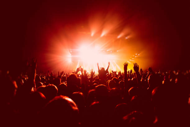A crowded concert hall with scene stage in red lights, rock show performance, with people silhouette, colourful confetti explosion fired on dance floor air during a concert festival stock photo
