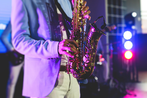 Concert view of saxophonist, a saxophone sax player with vocalist and musical band during jazz orchestra show performing music on a stage in the scene lights