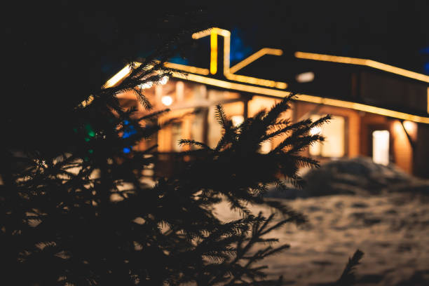 vista de una acogedora cabaña escandinava de madera casa de campo chalet cubierta de nieve cerca de la estación de esquí lodge en invierno con las luces de iluminación navideña encendidas, imagen cálida de la tarde - cabin snow finland lapland fotografías e imágenes de stock