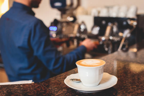 View of barista working at coffee machine in coffee house bar, bartender barman making cappuccino or latte, bartender preparing coffee drink at the cafe counter
