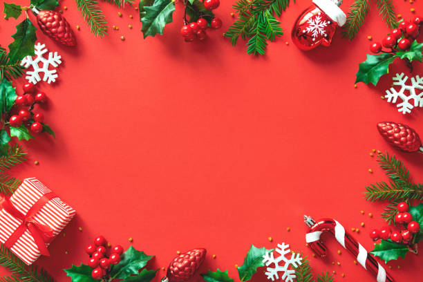 istock Christmas tree branches, holly berries and decorations on red background with space for text 1440938998
